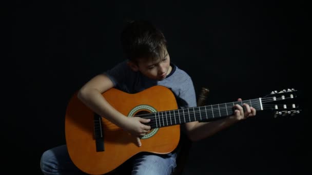 アコースティックギターを学ぶ少年 少年はアコースティックギターを練習している — ストック動画