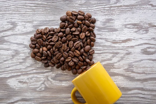 Heart shape made of coffee beans and yellow coffee. Wooden background