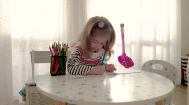 Cute little girl enjoys painting. Girl drawing and coloring picture with color pencil in her room at home