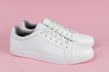 Pembe arka planda bir çift yeni beyaz spor ayakkabı.