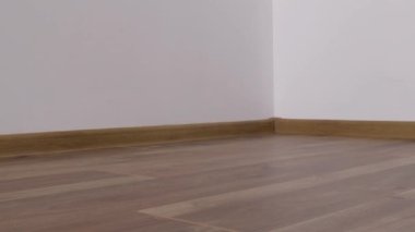 Laminated wood floor with white wall. Empty room with new laminate in new apartment