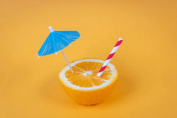 Orange cut in half with umbrella and straw on yellow background. Summer concept.