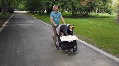 Parkta iki çocuklu bir baba. İkiz bebek arabasını iten adam..