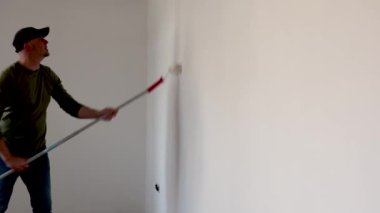 Daireyi yenilerken duvarları tekerlekli sandalyeyle boyayan adam. Ressam bir silindirle duvar boyuyor. Yeni Ev