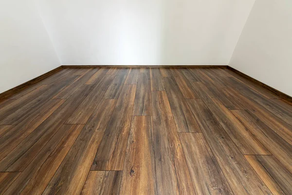 Laminated wood floor with white wall. Empty room with floating laminate in new apartmen
