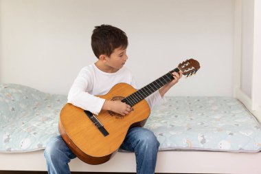 Çocuk akustik gitar çalmayı öğreniyor. Oğlan odasında akustik gitar çalışıyor.