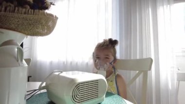 Astım spreyi maskesi takmış şirin bir kız. Evde solunum prosedürü uygulanıyor. Çocuk nebulizörle solunum terapisi görüyor..
