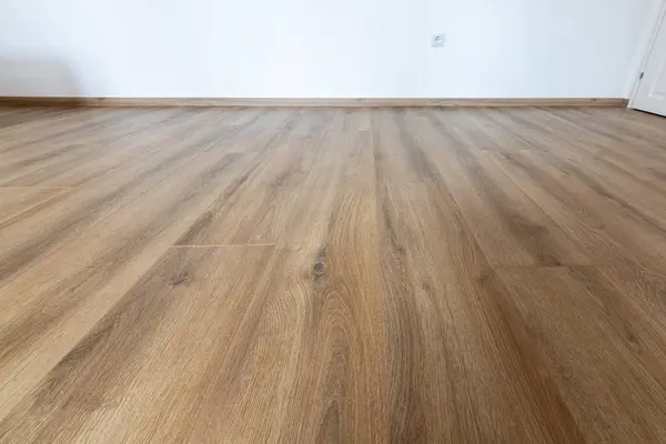 Laminated wood floor with white wall. Empty room with floating laminate in new apartmen
