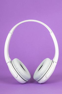 Wireless white headphones on purple background. Music concept. Earphones on purple background. 
