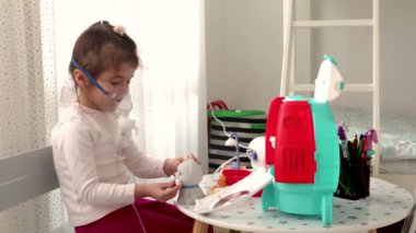 Astım spreyi maskesi takmış şirin bir kız. Oyuncaklarla oynamak. Evde solunum prosedürü uygulanıyor. Çocuk nebulizörle solunum terapisi görüyor.. 