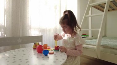 Küçük kız evde plastik oyuncaklarla oynuyor. Küçük kız oyuncak bardaktan çay içiyor.