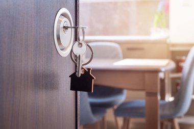 Anahtarı ve ev şeklindeki anahtarlığı olan yeni bir eve açılan kapı. İpotek, yatırım, gayrimenkul, mülk ve yeni konut kavramı