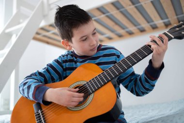 Çocuk akustik gitar çalmayı öğreniyor. Oğlan odasında akustik gitar çalışıyor.