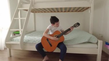 Çocuk akustik gitar çalmayı öğreniyor. Oğlan odasında akustik gitar çalışıyor.
