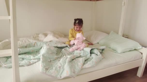 Утром Просыпается Маленькая Девочка Игрушкой Постели Счастливая Девушка Пижаме Сидит — стоковое видео