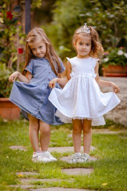 Tatlı çocuklar, prenses elbiseleri içindeki mutlu küçük kızların portresi. Güzel bahçedeki iki küçük kız kardeş