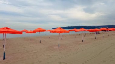 Şemsiyeli boş bir sahil. Yazın boş sahilde bir sürü turuncu şemsiye var.