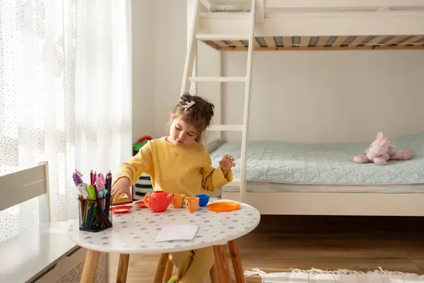 小女孩在家里的室内玩塑料玩具厨房 免版税图库图片