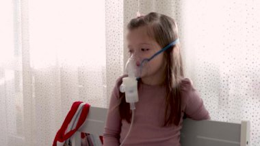 Astım spreyi maskesi takmış şirin bir kız. Evde solunum prosedürü uygulanıyor. Çocuk nebulizörle solunum terapisi görüyor..