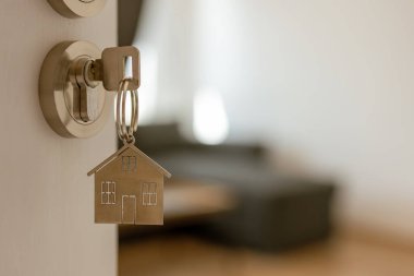 Anahtarı ve ev şeklindeki anahtarlığı olan yeni bir eve açılan kapı. İpotek, yatırım, gayrimenkul, mülk ve yeni konut kavramı