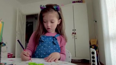 Şirin küçük kız resim yapmayı seviyor. Evindeki odasında renkli kalemle resim ve boyama yapan kız.