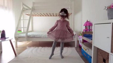 Kafasında tacı olan küçük prenses elbisesini gösteriyor. Taç takan genç kız.