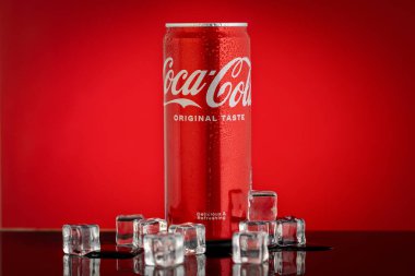 Varna, BULGARIA - 22 Nisan 2024: Klasik Coca Cola tadı, kırmızı su damlaları ve kırmızı zemin üzerinde buz olan kırmızı kutu