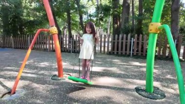 Küçük mutlu kız parkta eğleniyor. Sallanıyor salıncakta. 
