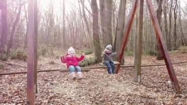 İki küçük kız ormanda salıncakta sallanıyor.