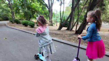 Parkta scooter süren iki kız. Çocuklar dışarıda mobiletlerle eğleniyor..