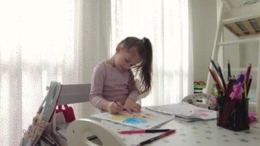 Cute little girl enjoys painting. Girl drawing and coloring picture with color pencil in her room at home