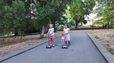 Parkta scooter süren iki kız. Çocuklar dışarıda mobiletlerle eğleniyor.. 
