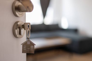 Anahtarı ve ev şeklindeki anahtarlığı olan yeni bir eve açılan kapı. İpotek, yatırım, gayrimenkul, mülk ve yeni konut kavramı