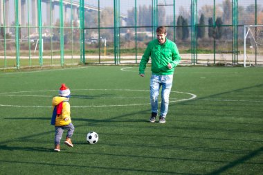 Babası küçük oğluyla eğleniyor, futbol oynuyor, parkta futbol oynuyor.