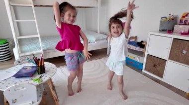 İki küçük kız çocuk odasında birlikte oynayarak eğleniyorlar. Mutlu şirin kız kardeşler ya da evde dans eden arkadaşlar