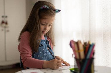 Cute little girl enjoys painting. Girl drawing and coloring picture with color pencil in her room at home