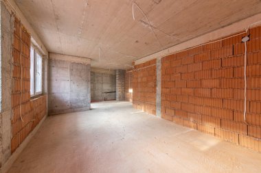 İnşaat halindeki binanın içinde bitmemiş bir oda. Tuğla kırmızı duvarlar. Yeni ev.