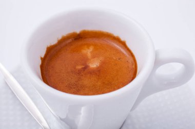 Beyaz arka planda kaşıkla beyaz bir fincan kahve.