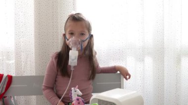 Astım spreyi maskesi takmış şirin bir kız. Evde solunum prosedürü uygulanıyor. Çocuk nebulizörle solunum terapisi görüyor..