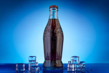 Varna, BULGARIA - 22 Nisan 2024: Mavi zemin üzerinde su damlaları ve buz bulunan klasik Coca Cola şişesi