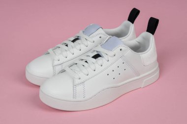 Pembe arka planda bir çift yeni beyaz spor ayakkabı. Kadın spor ayakkabıları..