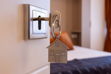 Anahtarı ve ev şeklindeki anahtarlığı olan yeni bir eve açılan kapı. İpotek, yatırım, gayrimenkul, mülk ve yeni konut kavramı