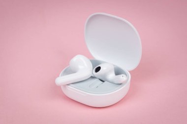 Pembe arka planda beyaz kablosuz kulaklıklar. Yeni kulaklıklar. Yeni teknolojiler.