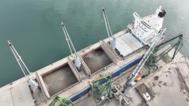 Limandaki vinçlerle ayçiçeği taşıyan kuru kargo gemisi yükleniyor. Deniz kargo gemisinin ambarına hava görüntüsü yükleniyor