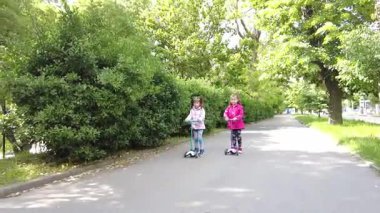 Parkta scooter süren iki kız. Çocuklar dışarıda mobiletlerle eğleniyor..