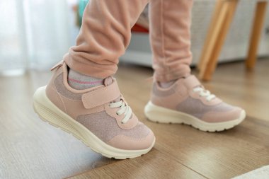 Cırt cırt cırtlı ve bağcıklı şık pembe ayakkabılar giyen bir çocuğun kapalı bir yerde, ahşap bir zeminde dikilirken yakın çekimi. Aktif günlük çocuk ayakkabıları için rahat ve modaya uygun.
