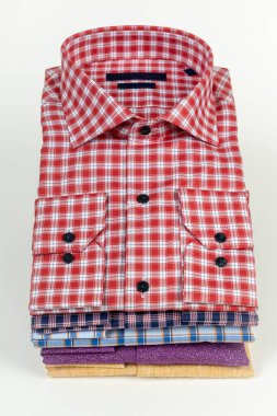 Üzerinde kırmızı bir ekose gömlek olan çeşitli renk ve desenlerde katlanmış erkek gömlekleri yığını. Moda, giyim mağazaları ve giyim reklamları için mükemmel.