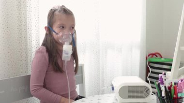 Astım spreyi maskesi takmış şirin bir kız. Evde solunum prosedürü uygulanıyor. Çocuk nebulizörle solunum terapisi görüyor..