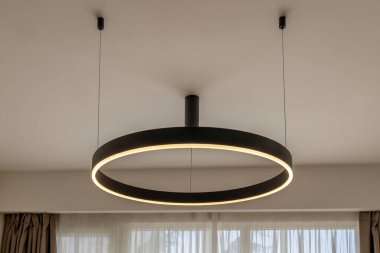 Çağdaş bir iç mekanda tavandan sarkan parlak siyah çerçeveli modern dairesel LED kolye. Şık bir ev ortamında minimalist aydınlatma armatürü..