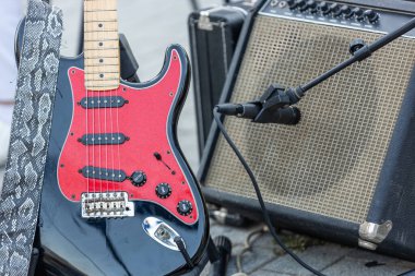 Elektro gitarın, önünde mikrofon olan vintage bir amfiye yaslanmış halinin yakın çekimi. Canlı müzik ve rock performans konsepti.
